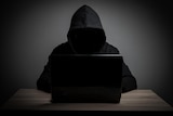 Person in dark tracksuit sitting at a laptop screen - you can't see their face. 