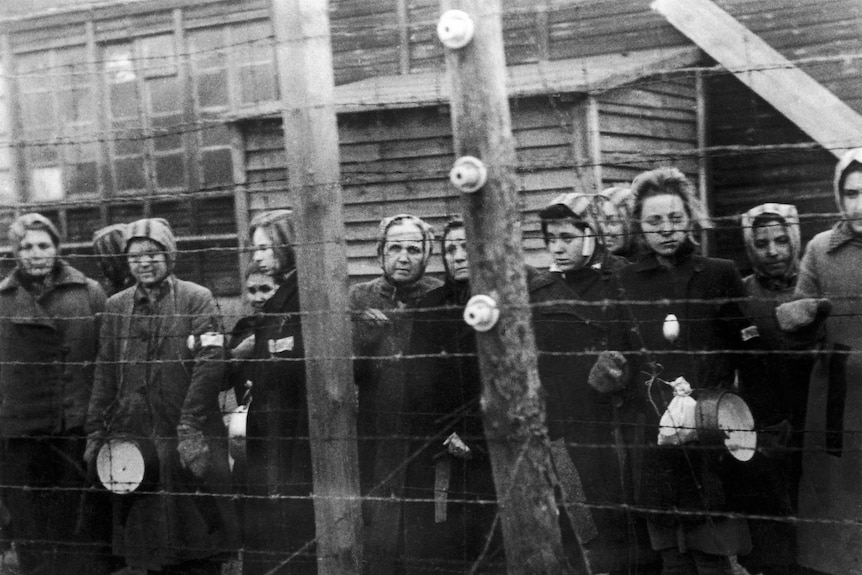 Archival photo of women standing behind wire at a concentration camp in Germany in WWII.