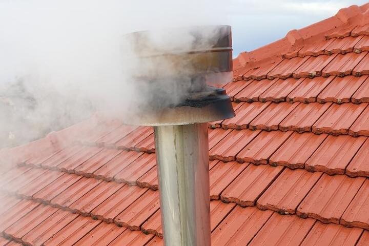 Chimney with smoke coming out of it over a red tiled roof.