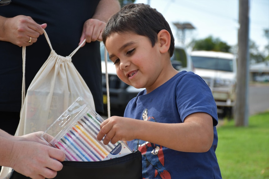 A young child pull a pack of crayons out of a bag.