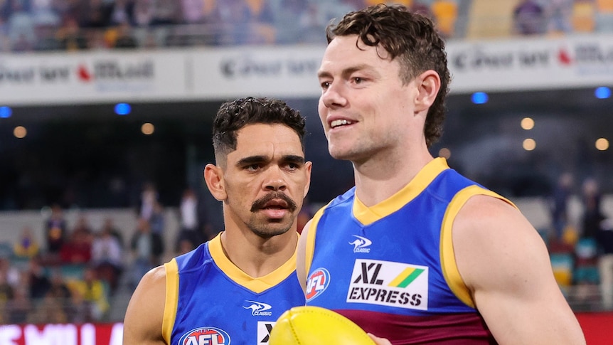 Two Brisbane Lions AFL players prepare to run onto the field.