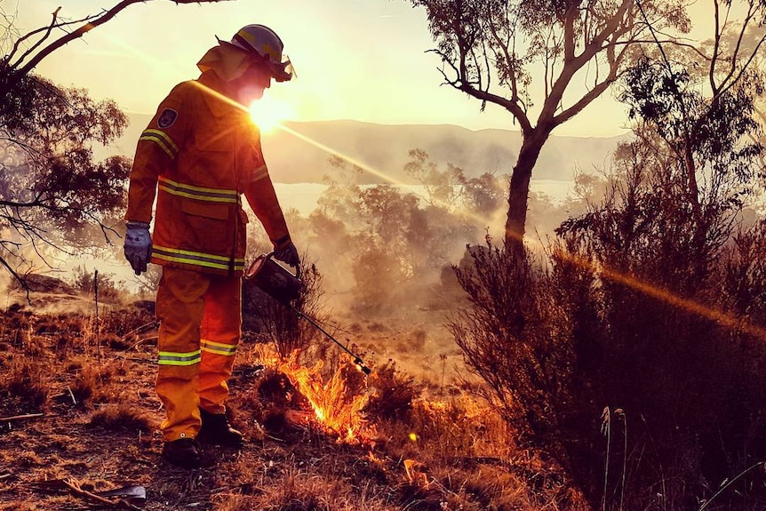 Man in orange safety wear and helmet manages a small burn off