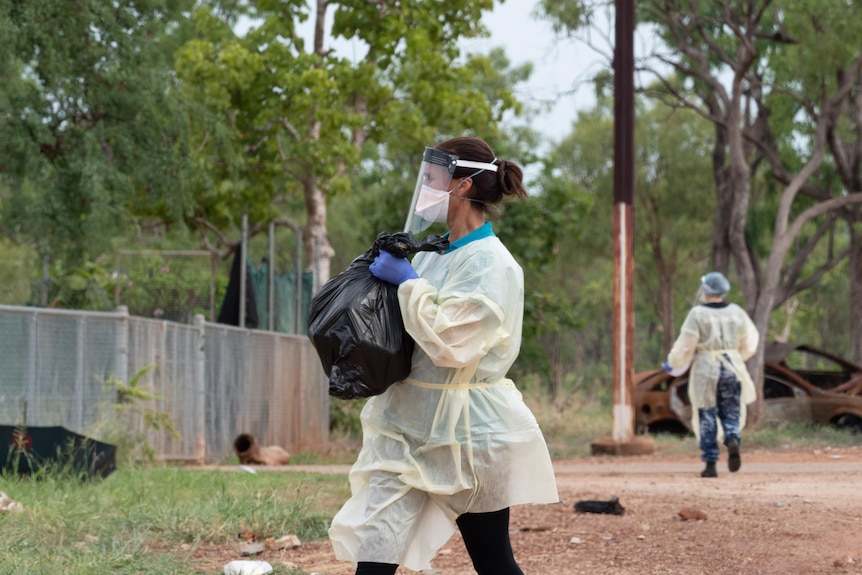 A woman wearing PPE carries a bag in bushland