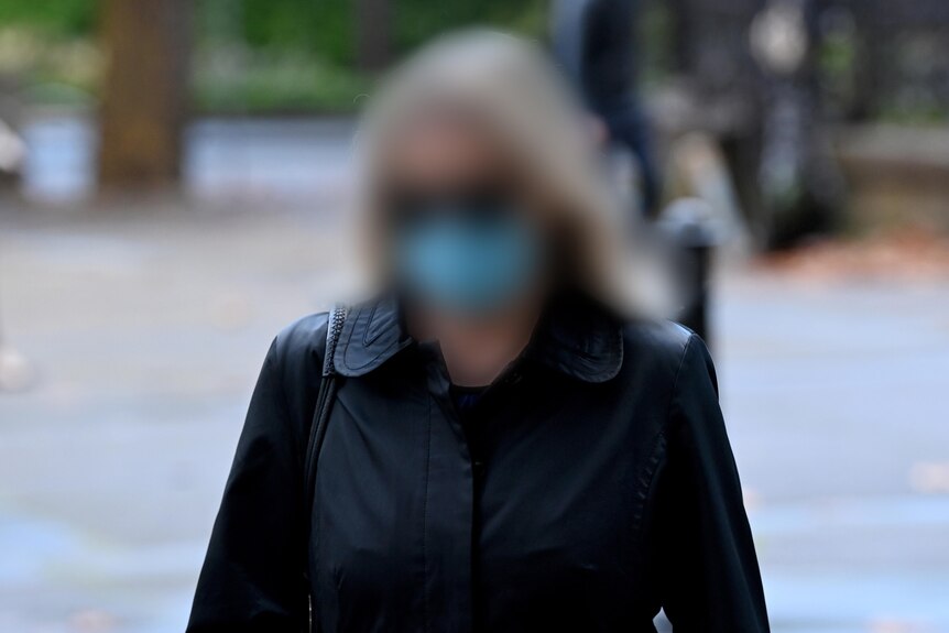 A woman wearing a black coat and mask with her face blurred