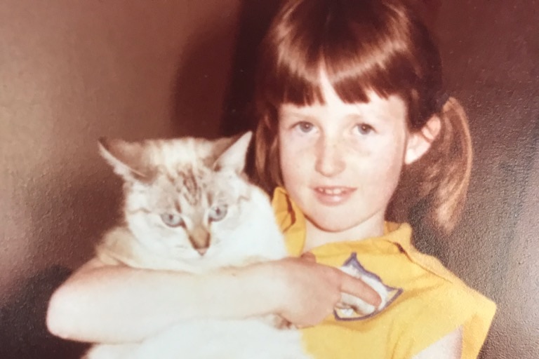 A old film photo of a girl holding  a cat at smiling at the camera