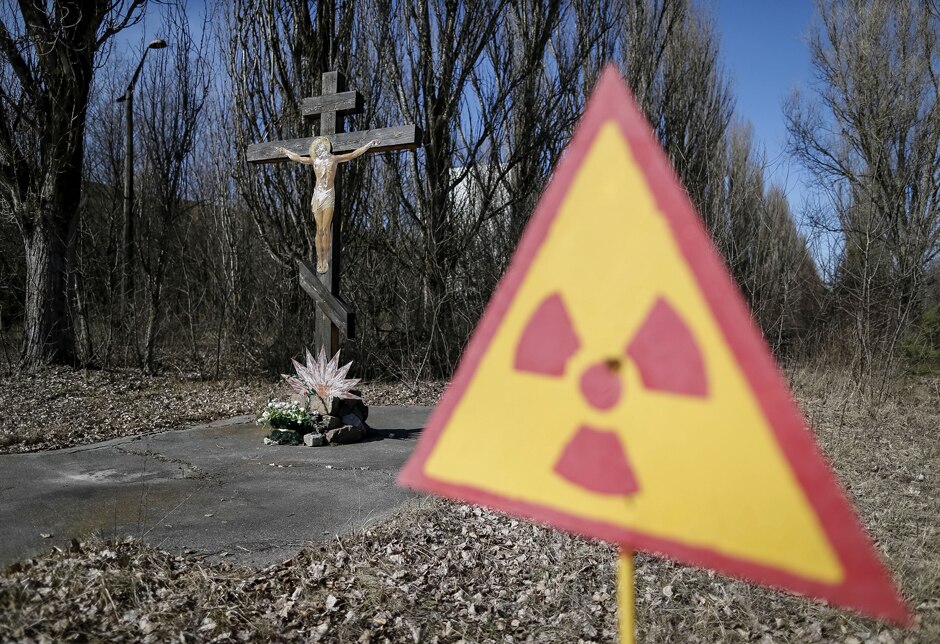 A cross with a crucifix stands next to a radiation warning sign near the Chernobyl power plant.