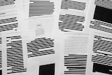 Pieces of paper with large swathes of text blacked out sit n a pile together