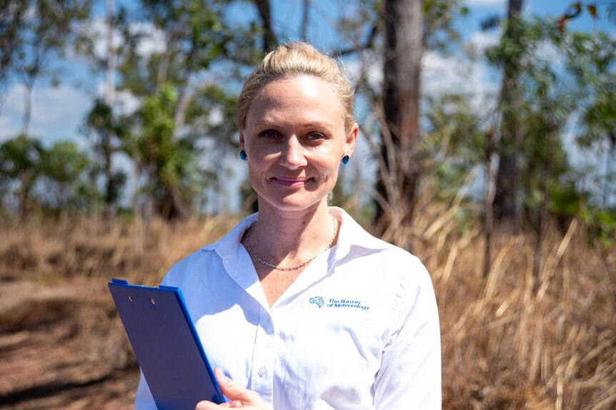 A woman stands in bushland with a blue clip board. 