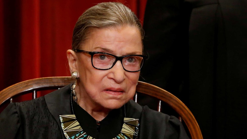 Ruth Bader Ginsburg sitting in a chair wearing justice robes and a statement necklace