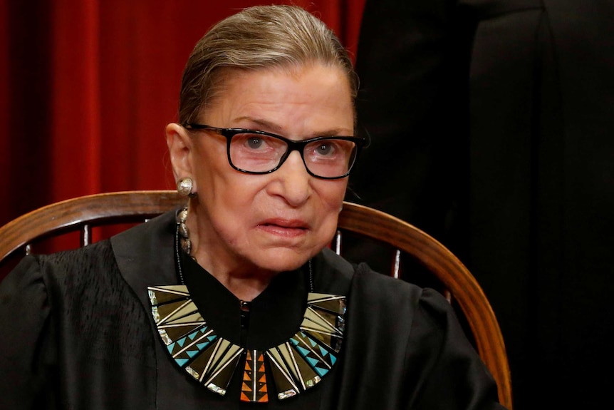 Ruth Bader Ginsburg sitting in a chair wearing justice robes and a statement necklace