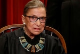 Ruth Bader Ginsburg sitting in a chair wearing justice robes and a statement necklace