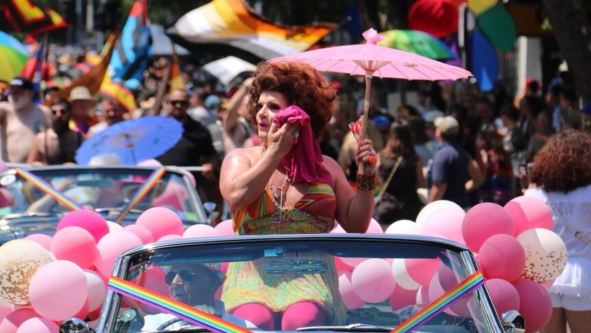 A participant of the Melbourne Midsumma Festival march sits in an open car holding an sun umbrella.