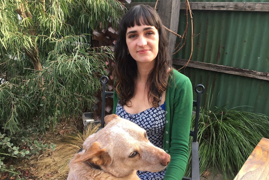 Orlaith Belfrage smiles at the camera with her dog Red at her feet.