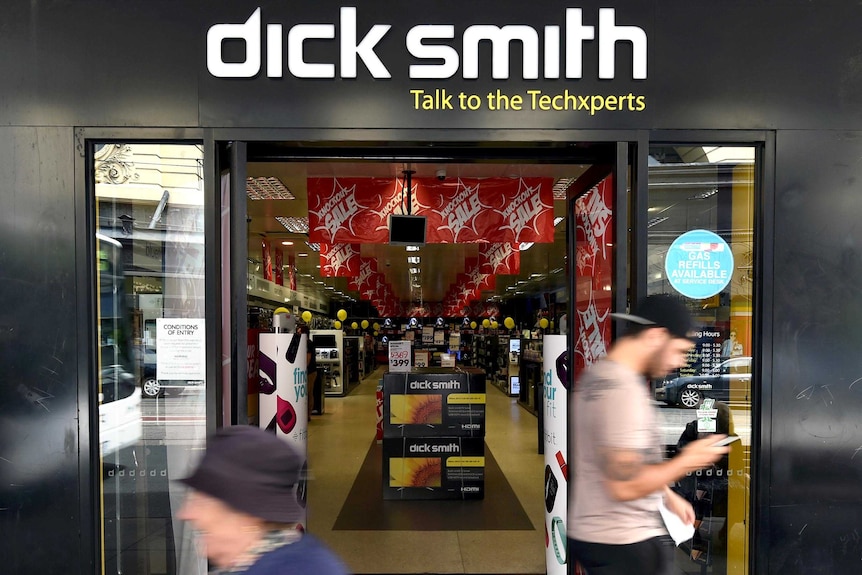 People, blurred by their movement, walk past the front of a Dick Smith store, with the Dick Smith logo above the door.