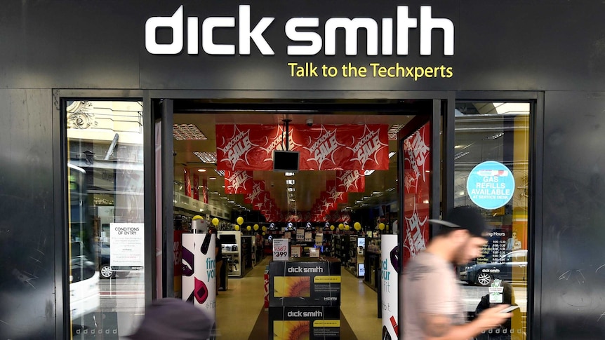 People, blurred by their movement, walk past the front of a Dick Smith store, with the Dick Smith logo above the door.