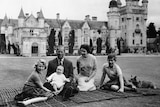 A black and white photo of Queen Elizabeth and Philip sitting on a picnic blanket with their kids and dog