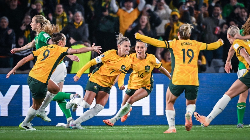 The Matildas celebrate by running towards each other near the goal.