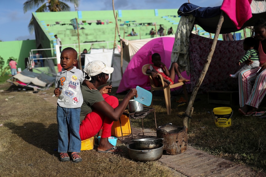Woman and a small boy sit in front of a makeshift tent structure 