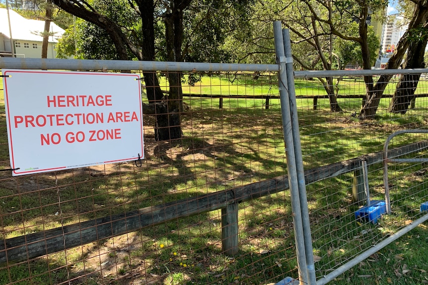Steel temporary fence around parkland and wooden fence marking bora ring. Sign says "Heritage Protected Area No Go Zone"