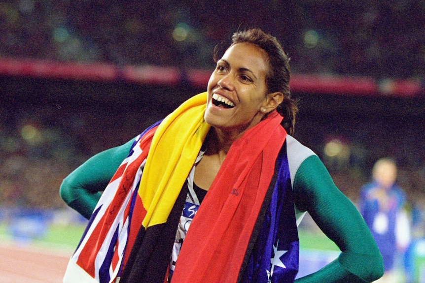 Cathy Freeman smiling with the Aboriginal and Australian flag draped around her neck.