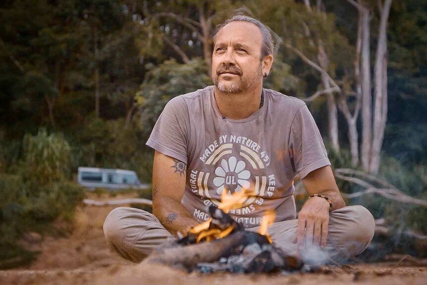 A man sits next to a small camp fire