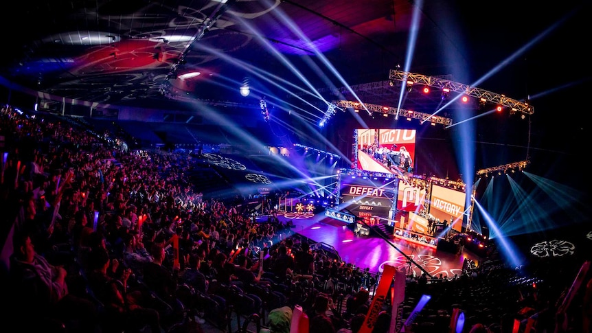 The inside of Rod Laver Arena lit up by lights and lasers as the crowd cheers during an esports game