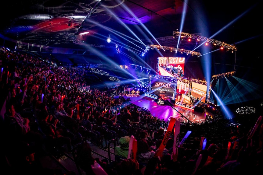 The inside of Rod Laver Arena lit up by lights and lasers as the crowd cheers during an esports game