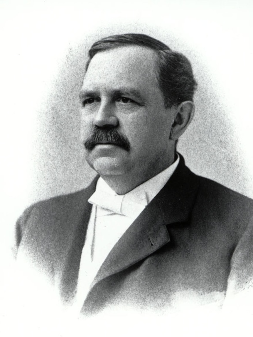 Black and white photo of a mustached man in formal dress.