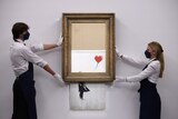 Two people hold a Banksy art on the wall 