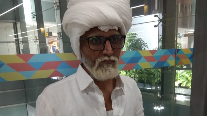 A man who appear to be an elderly, dressed in white, with a white beard and turban.