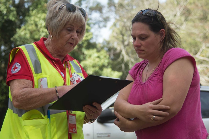 A woman with a clipboard and a hi-vis vest speaks to a woman with a pink shirt