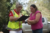 A woman with a clipboard and a hi-vis vest speaks to a woman with a pink shirt