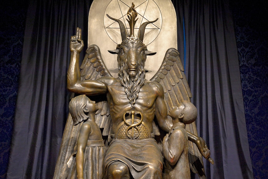 Imposing statue of Baphomet flanked by children with pentagram in the background