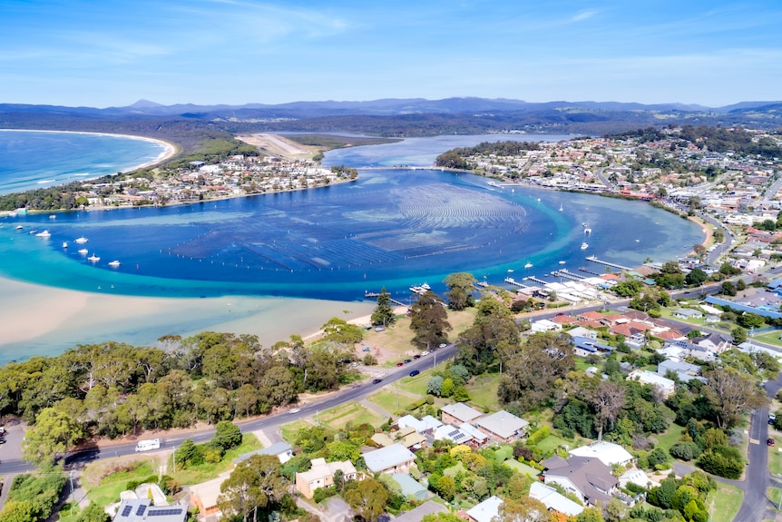 a drone shot of merimbula including houses and a lake near the ocean