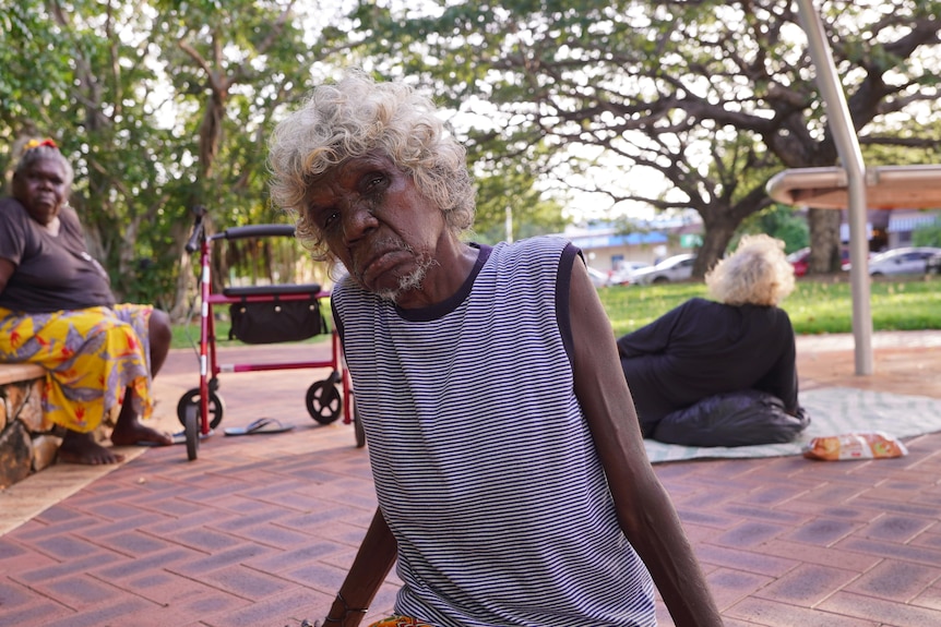 Three Indigenous people sitting in a park, with their possessions scattered around them