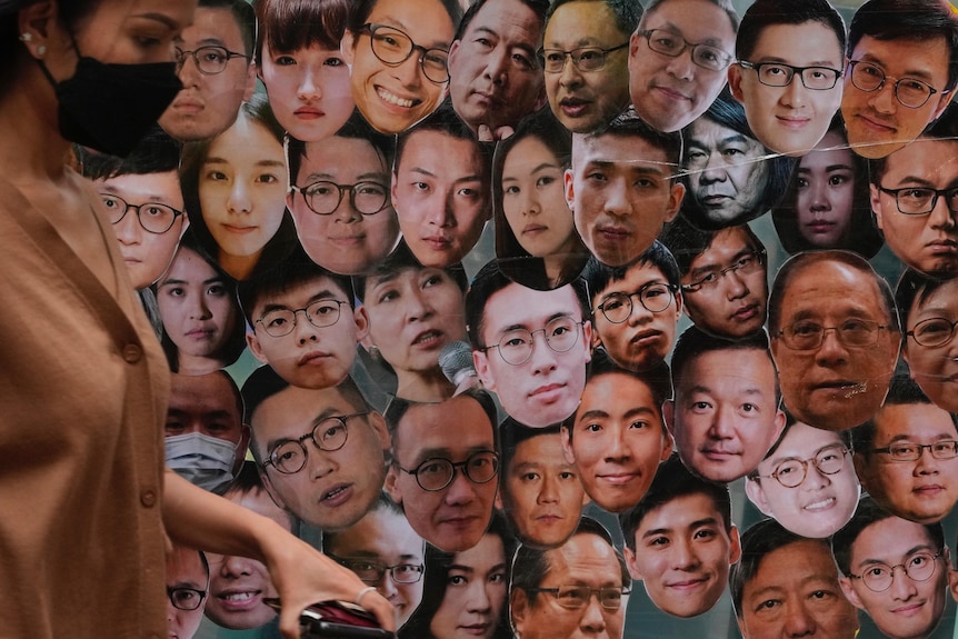 Photos of faces hang on a wall. There are more than 40 people pictured. 