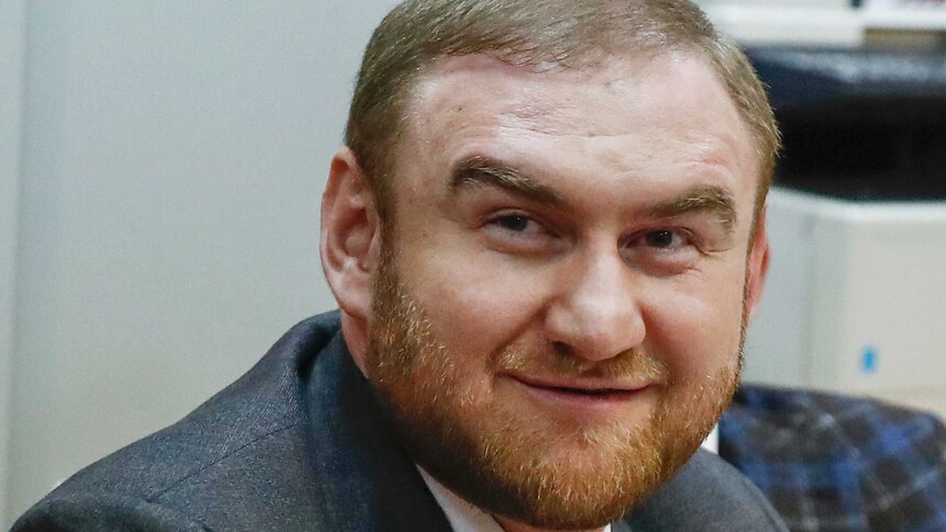 Russian lawmaker Rauf Arashukov smiles during hearings in a court in Moscow. He has a short red beard and wears a suit.