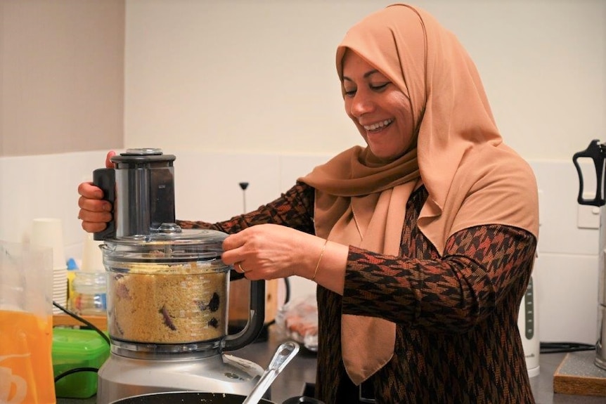 A woman mixes food in a blender while smiling