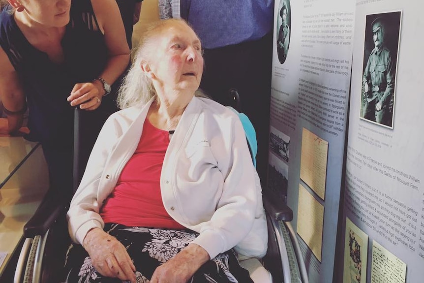 Old woman in a wheelchair looks at a photograph on the wall. Eunice Gilmour is the oldest survivor of the Fryer brothers.