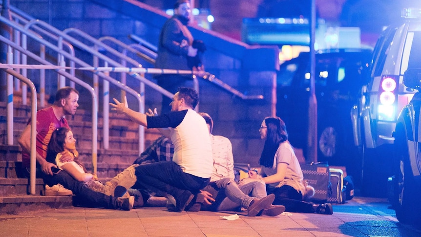 Parents and their children sit on steps near Manchester Arena.