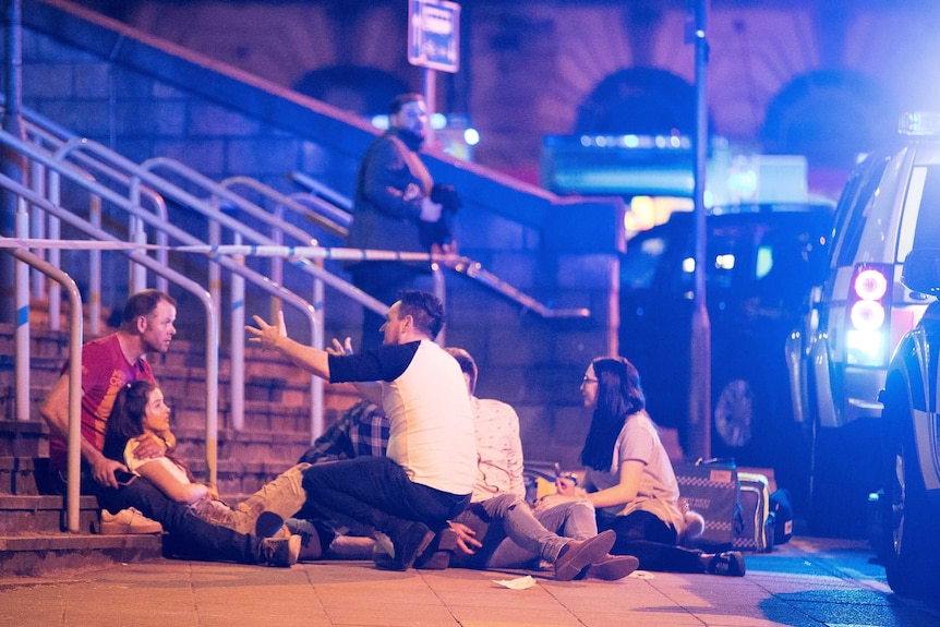 Parents and their children sit on steps near Manchester Arena.