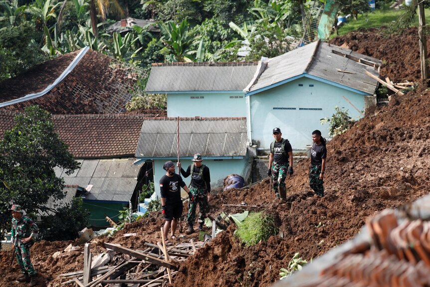 Indonesian Army officers stand on dirt left behind by a landslide. 
