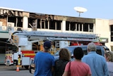 Five people, pictured from behind, look at the burnt-out second storey building
