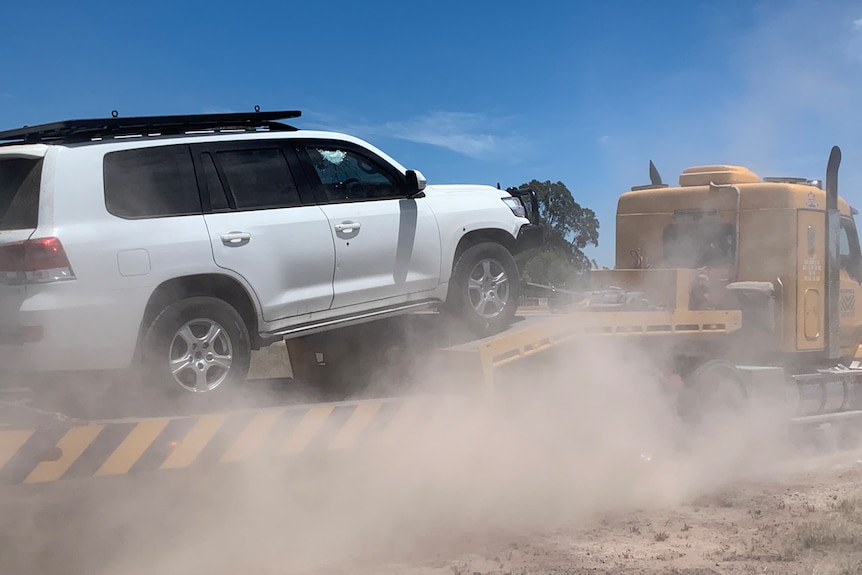 A white Toyota Landcruiser is towed in the dirt. Bullet holes can be seen in the side