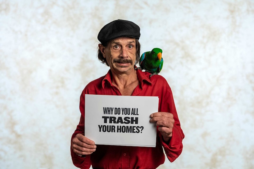Pierre Gawronski has a parrot sitting on his shoulder and he is holding a sign that reads "Why do you all trash your homes?"