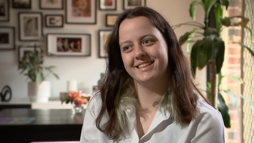 A teen with brown hair sits in her living room for an interview