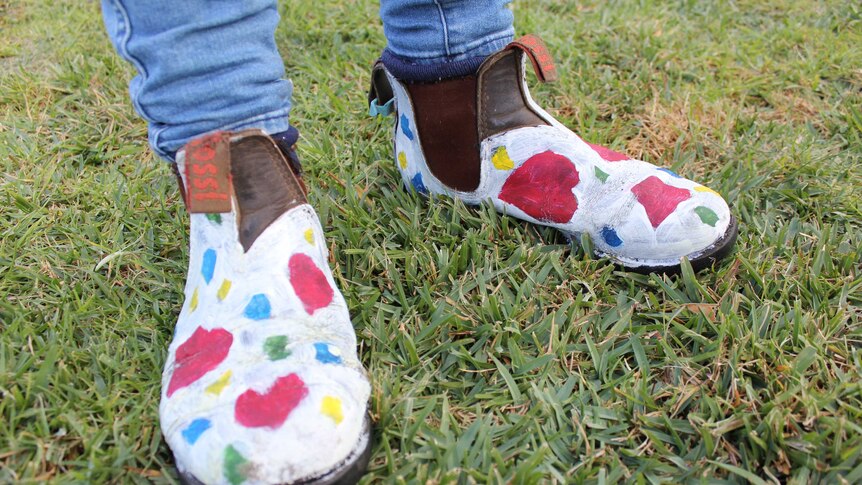 A close up shot of a pair of old work boots that have been painted white with multi coloured polka dots