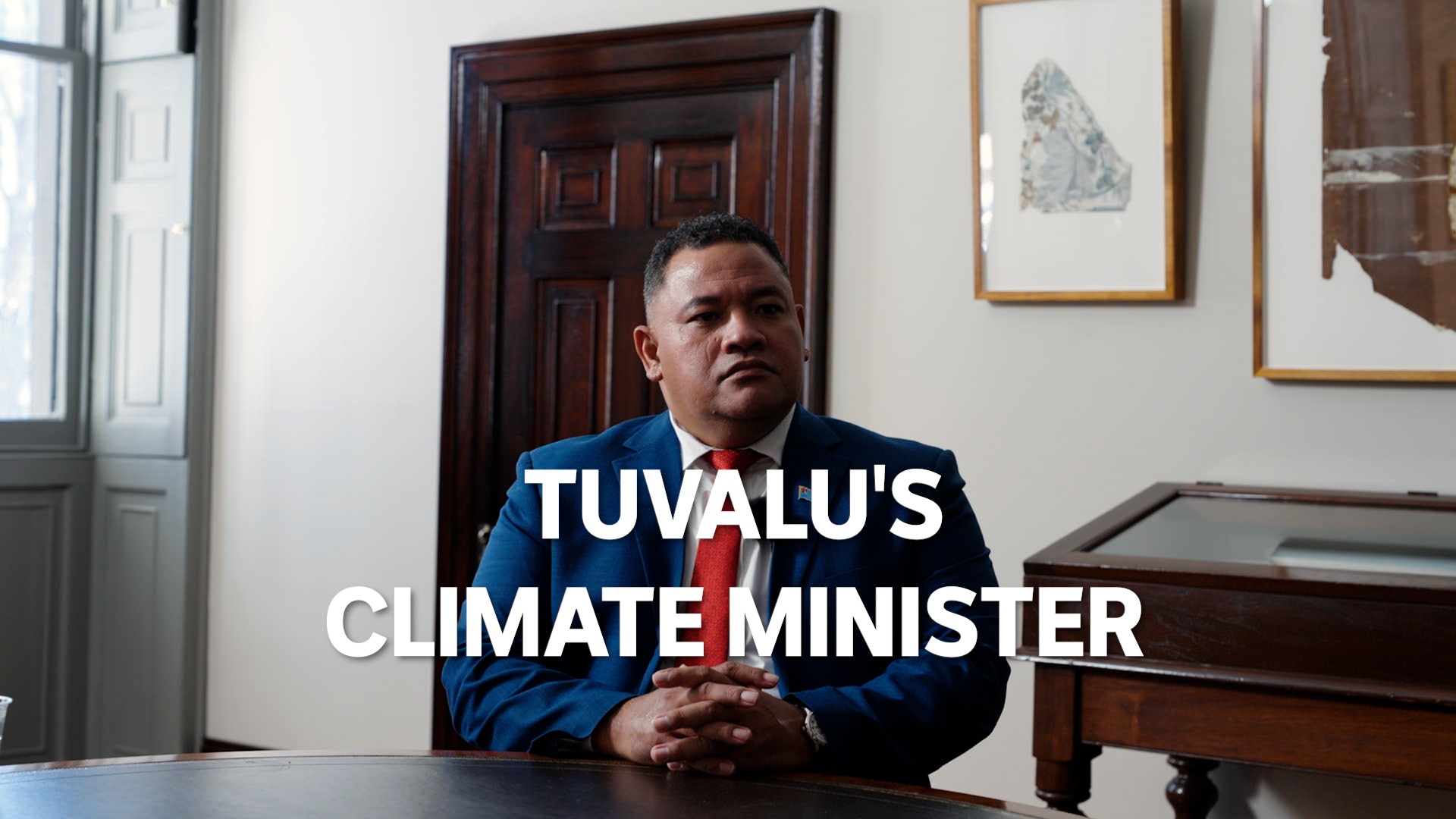 Dr Maina Vakafua Talia sits in a room in front of table, text overlay says 'Tuvalu's climate minister'