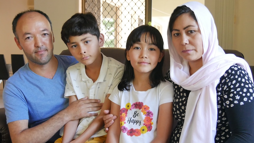 A man in a blue shirt, a boy in a yellow shirt, a girl and a woman in a head scarf sit together on a couch.