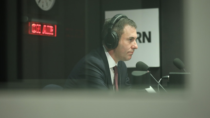 Chalmers sits inside a studio wearing headphones, a lit "on air" sign behind him.